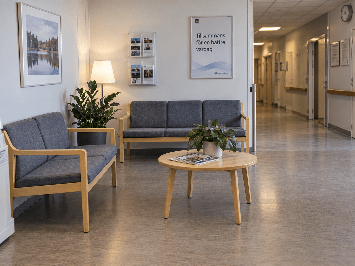 Väntrum med två soffor i grått tyg och ljust trä i en vårdkorridor